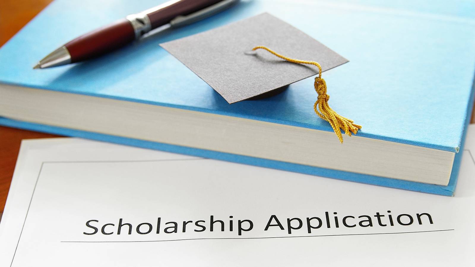 Paper scholarship application, with a book and miniture graduation cap on top