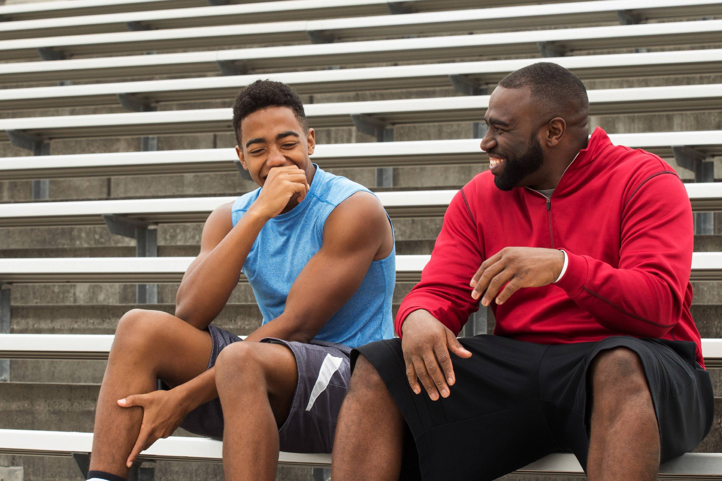 Two young men sitting in athletic gear on bleachers