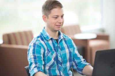 Student in blue button up shirt at a laptop