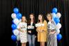 Students and sponsors on platform with black background and blue, white and silver balloons. 