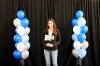 Student on platform with black background and blue, white and silver balloons. 