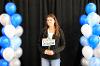 Student on platform with black background and blue, white and silver balloons. 