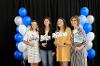 Students and sponsors on platform with black background and blue, white and silver balloons. 