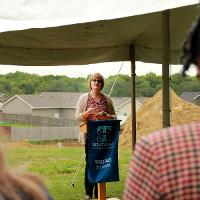 Woman at podium with STC banner in front and construction site in background.