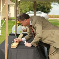 Man writing on a board placed on a table under a tent and sitting on a black tablecloth. 