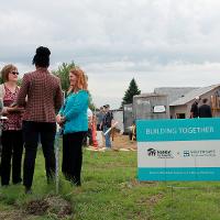 Partnership sign in foreground, people visiting and construction site in background. 