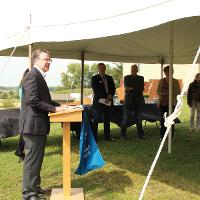 Man at podium with people in a tent behind him. 