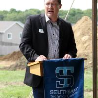 Man at podium with STC banner in front and construction site in background. 