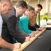 People writing on a board placed on a table under a tent and sitting on a black tablecloth, taken from an angle.