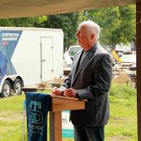 Man at podium with STC banner in front and construction site and mobile classroom in background.