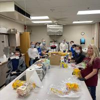 STC volunteers stand at large long table preparing sandwiches.